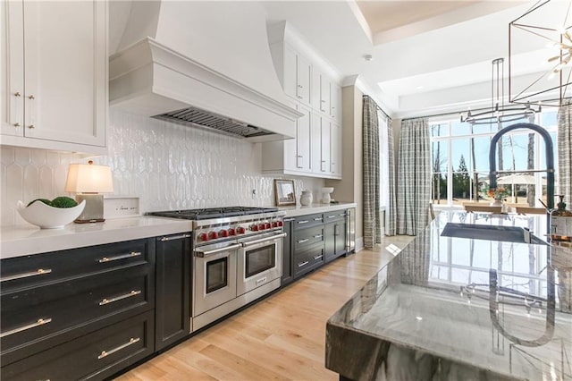 kitchen featuring light countertops, custom exhaust hood, white cabinets, and double oven range