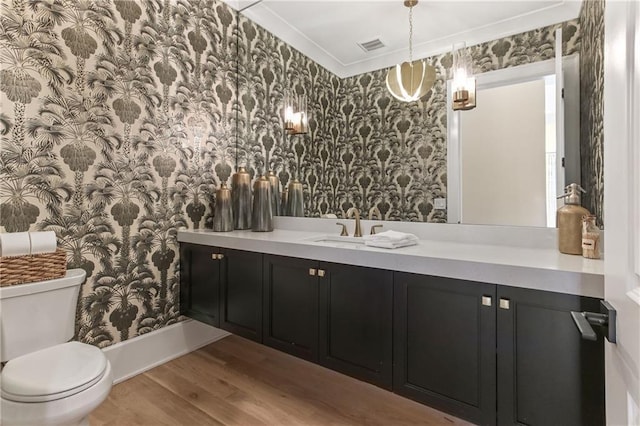 bathroom with toilet, wallpapered walls, wood finished floors, and vanity