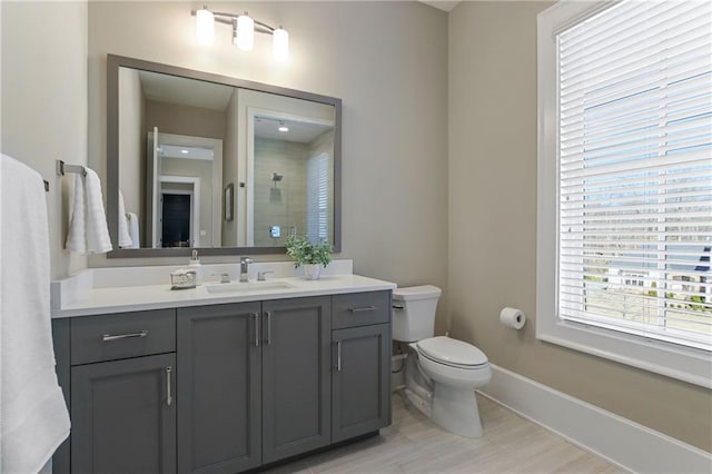 bathroom featuring baseboards, a tile shower, vanity, and toilet