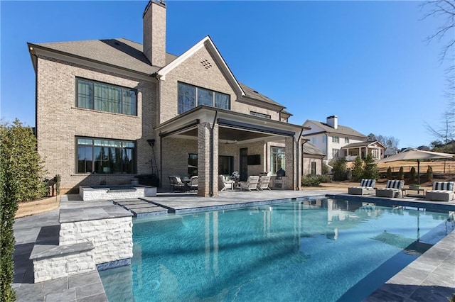 back of house featuring a patio, brick siding, a chimney, and a fenced in pool