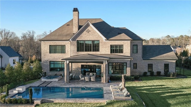 back of property with a chimney, a lawn, a patio area, an in ground hot tub, and an outdoor pool