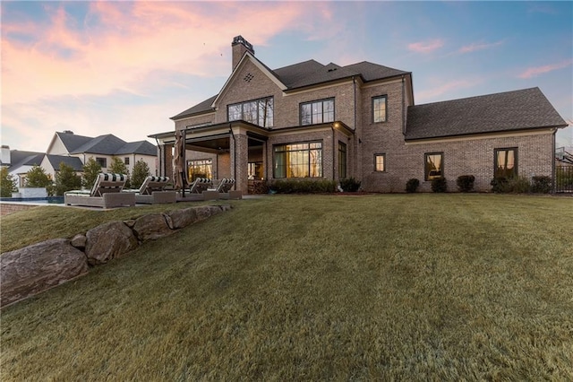 back of property with a yard, brick siding, a chimney, and a patio