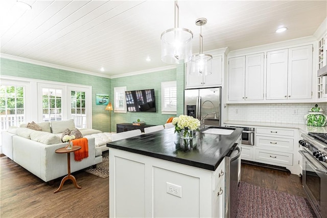 kitchen featuring appliances with stainless steel finishes, open floor plan, a sink, dark countertops, and dark wood-style flooring