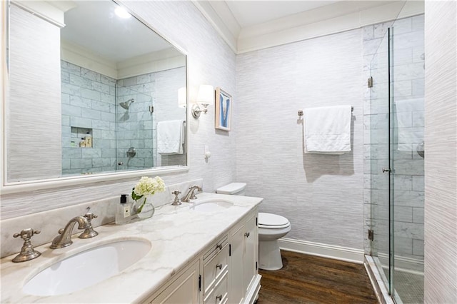 bathroom featuring a shower stall, toilet, wood finished floors, double vanity, and crown molding