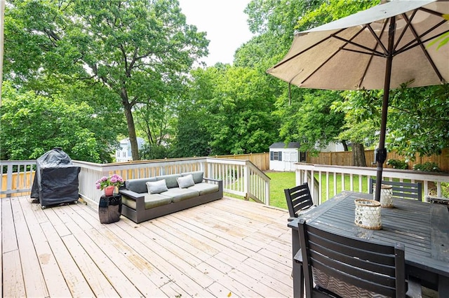 wooden terrace with a storage unit, an outbuilding, grilling area, outdoor dining area, and view of wooded area