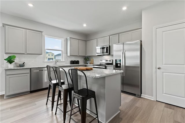 kitchen with a breakfast bar, decorative backsplash, light stone countertops, a kitchen island, and stainless steel appliances