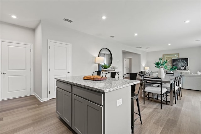 kitchen with gray cabinetry, light stone counters, light hardwood / wood-style floors, a kitchen bar, and a kitchen island