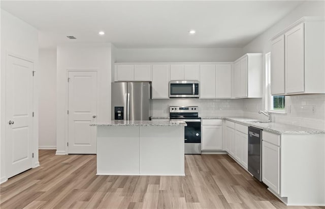 kitchen featuring a kitchen island, white cabinetry, appliances with stainless steel finishes, and light stone counters