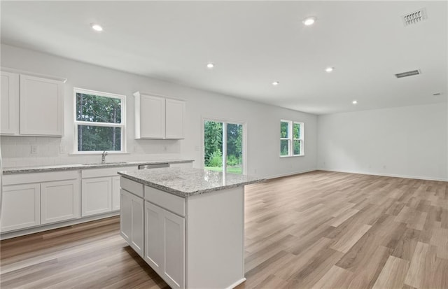 kitchen with a kitchen island, white cabinetry, light stone countertops, and tasteful backsplash