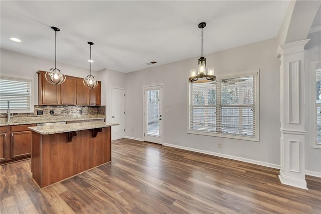 kitchen featuring dark hardwood / wood-style floors, decorative columns, a breakfast bar area, a center island, and light stone countertops