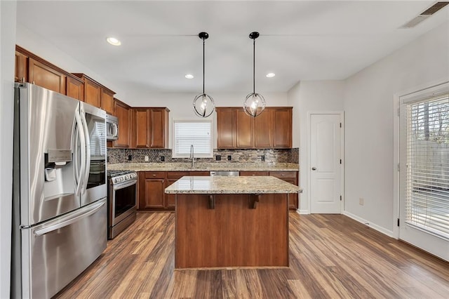 kitchen with decorative light fixtures, a center island, light stone counters, stainless steel appliances, and a healthy amount of sunlight