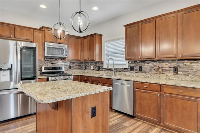 kitchen with sink, light hardwood / wood-style flooring, appliances with stainless steel finishes, a kitchen island, and pendant lighting