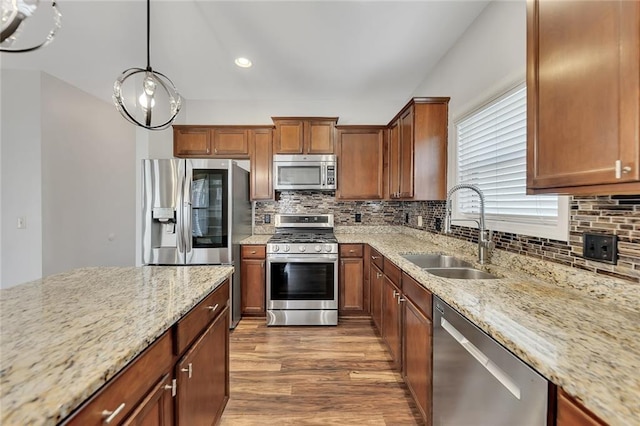 kitchen with light stone countertops, appliances with stainless steel finishes, sink, and decorative light fixtures