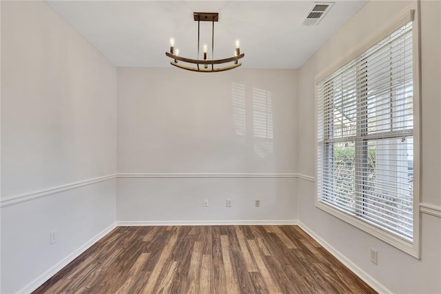 spare room featuring dark hardwood / wood-style flooring and a chandelier