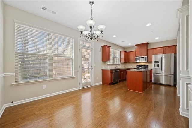 kitchen featuring hardwood / wood-style floors, backsplash, a chandelier, a center island, and stainless steel appliances