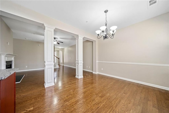 unfurnished dining area with ceiling fan with notable chandelier, dark hardwood / wood-style floors, and ornate columns