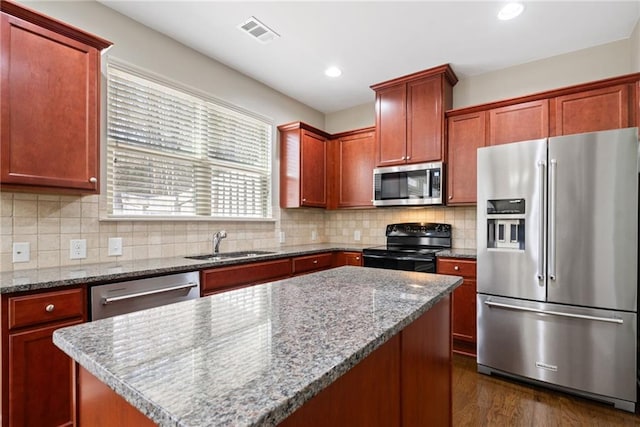 kitchen featuring sink, appliances with stainless steel finishes, a center island, light stone counters, and decorative backsplash