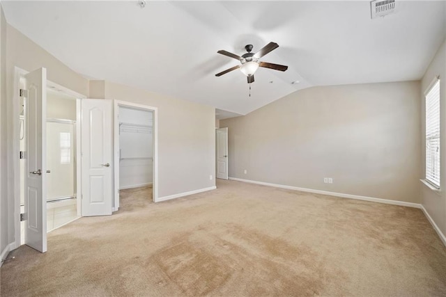 unfurnished bedroom featuring light carpet, a spacious closet, lofted ceiling, and ceiling fan