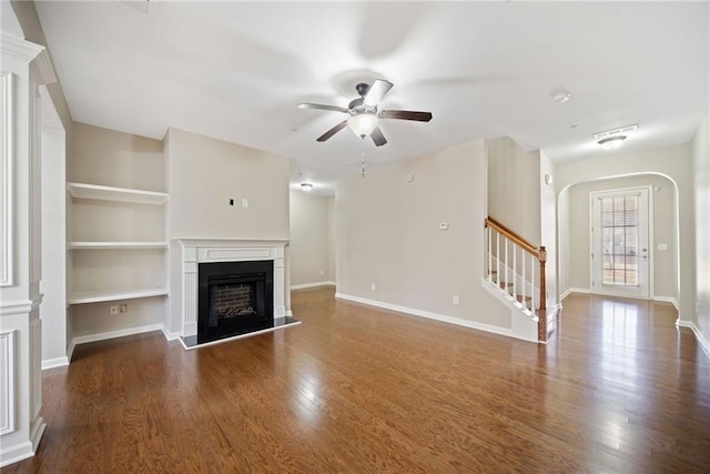 unfurnished living room with built in shelves, dark hardwood / wood-style floors, and ceiling fan