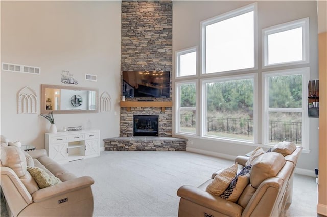 carpeted living room with baseboards, a towering ceiling, visible vents, and a fireplace