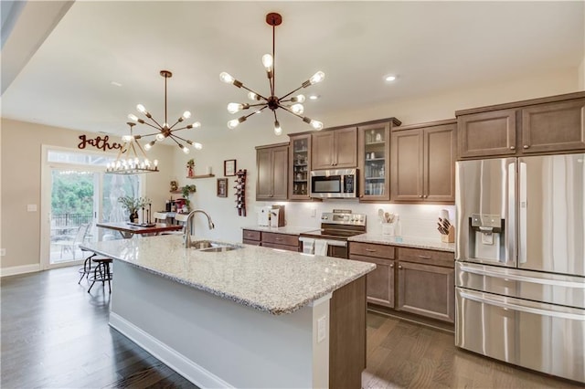 kitchen with stainless steel appliances, a sink, dark wood-style flooring, a notable chandelier, and light stone counters