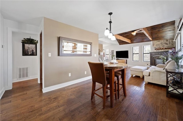 dining room with dark wood-style floors, a stone fireplace, visible vents, baseboards, and ceiling fan