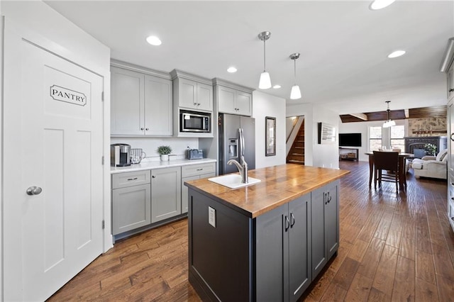 kitchen with gray cabinets, a sink, wood counters, appliances with stainless steel finishes, and open floor plan