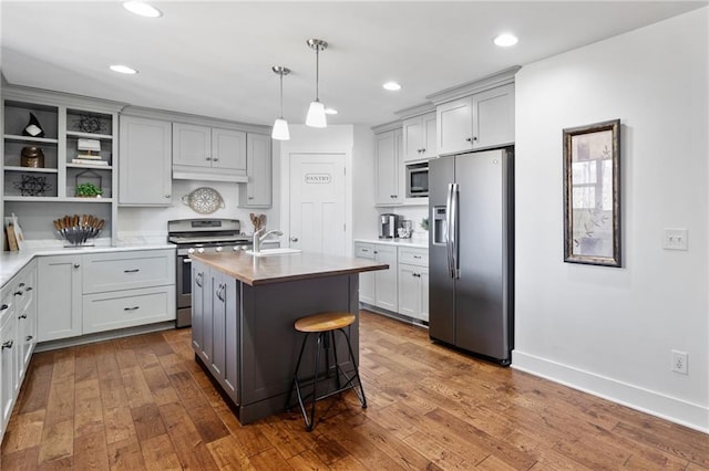 kitchen featuring open shelves, a sink, a center island with sink, appliances with stainless steel finishes, and gray cabinetry