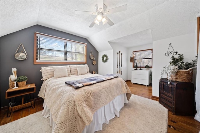 bedroom featuring a ceiling fan, wood finished floors, a textured ceiling, multiple windows, and lofted ceiling