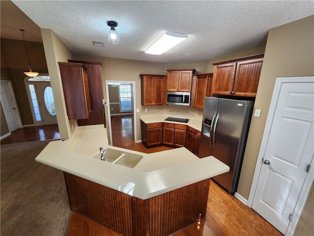 kitchen with appliances with stainless steel finishes, a peninsula, light countertops, light wood-style floors, and a sink