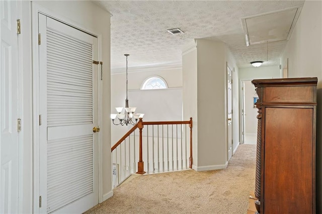 corridor with a textured ceiling, ornamental molding, a chandelier, and light colored carpet