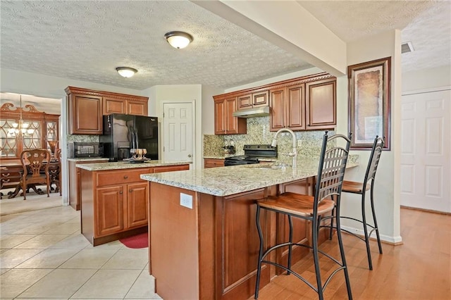 kitchen with light stone counters, light tile patterned floors, a textured ceiling, black appliances, and sink