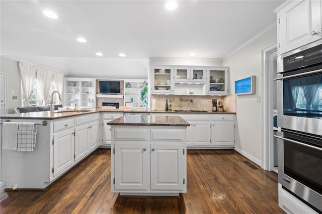 kitchen featuring glass insert cabinets, a center island, stainless steel double oven, decorative backsplash, and dark wood-style flooring