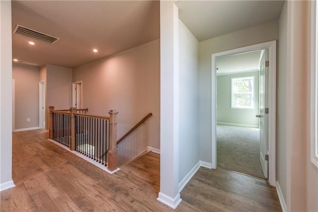 corridor with baseboards, visible vents, an upstairs landing, and wood finished floors