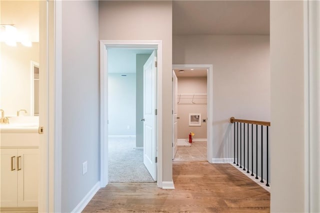 corridor featuring light wood-type flooring, a sink, and baseboards