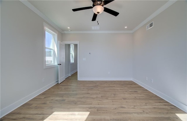 empty room featuring baseboards, light wood-type flooring, visible vents, and crown molding