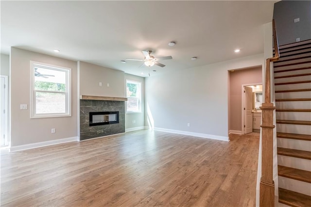 unfurnished living room with stairway, a glass covered fireplace, ceiling fan, light wood-type flooring, and baseboards