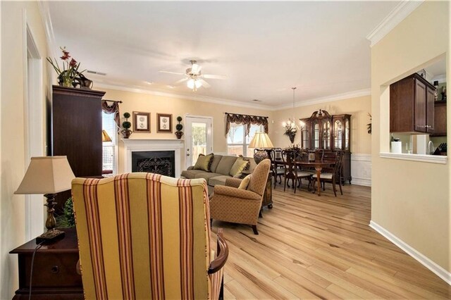 living area with a ceiling fan, a fireplace, baseboards, light wood-style floors, and ornamental molding