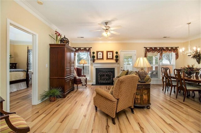 living room with a fireplace with flush hearth, light wood-type flooring, ceiling fan with notable chandelier, visible vents, and ornamental molding