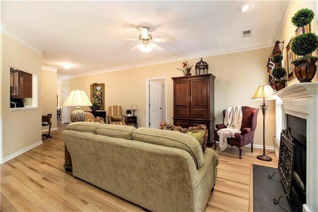 living area with crown molding, light wood-type flooring, baseboards, visible vents, and ceiling fan