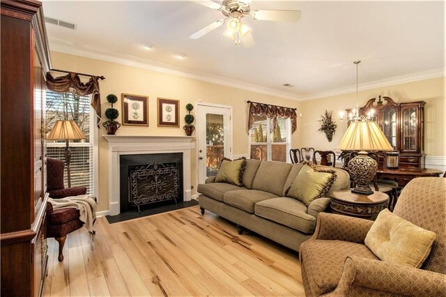 living area with a ceiling fan, visible vents, crown molding, and light wood-type flooring