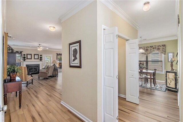 hallway with light wood finished floors, baseboards, and crown molding