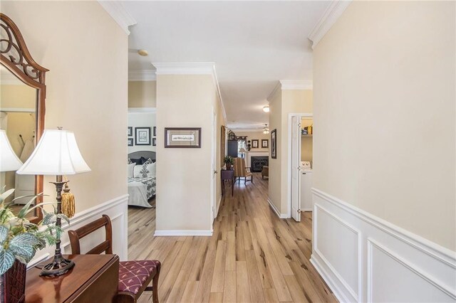 hall with a decorative wall, crown molding, light wood-style floors, and wainscoting