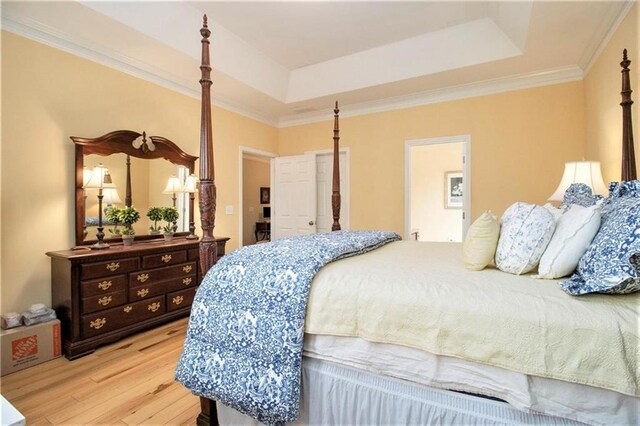 bedroom featuring light wood finished floors, crown molding, and a raised ceiling