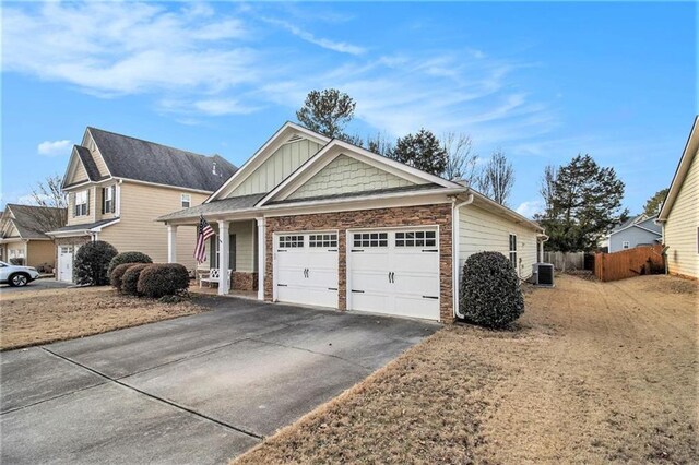 view of front of home with driveway, stone siding, central air condition unit, fence, and a garage