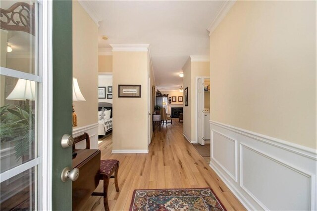 hallway with a wainscoted wall, light wood-type flooring, a decorative wall, and ornamental molding