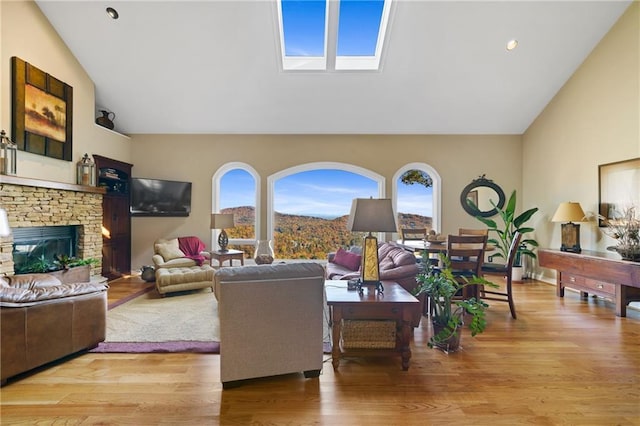living area with high vaulted ceiling, plenty of natural light, a stone fireplace, and light wood finished floors