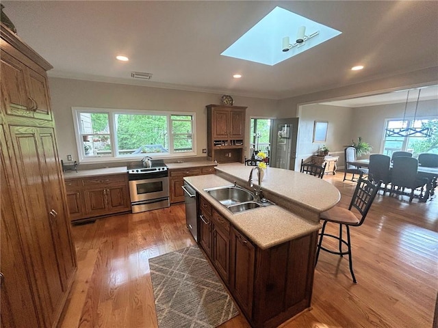 kitchen with appliances with stainless steel finishes, a sink, a center island with sink, light countertops, and plenty of natural light