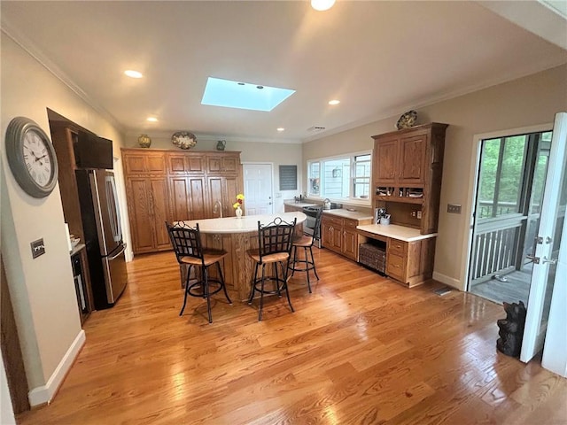 kitchen featuring freestanding refrigerator, a skylight, a kitchen bar, crown molding, and healthy amount of natural light