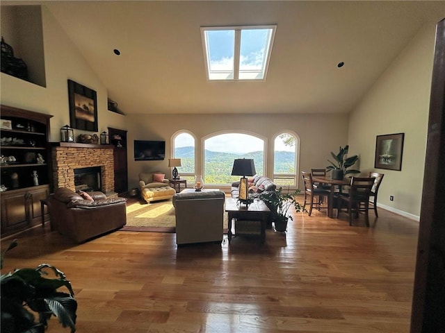 living area featuring high vaulted ceiling, wood finished floors, a fireplace, and a skylight